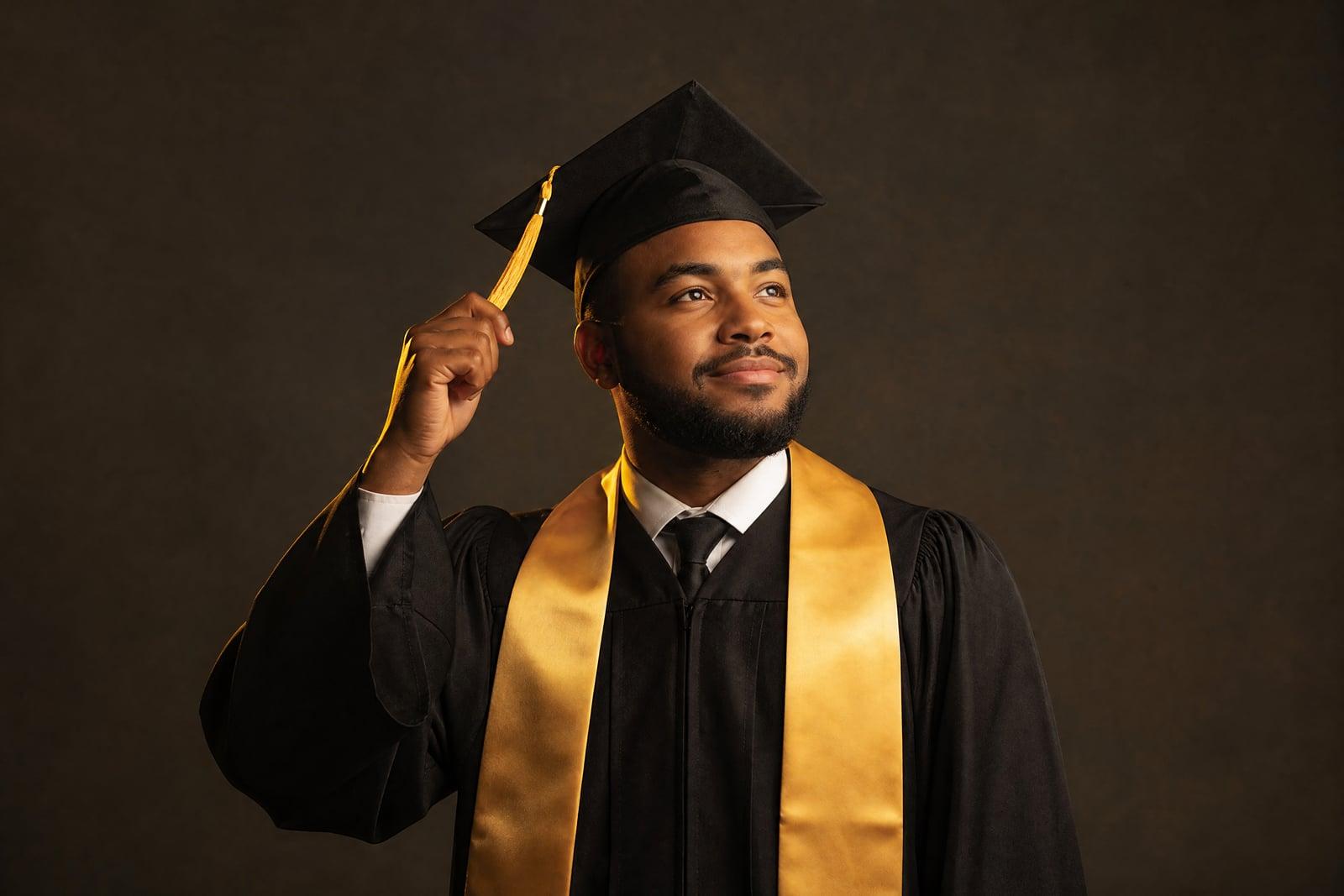Graduation Photo portrait of a graduate in cap and gown with a gold stole, studio backdrop