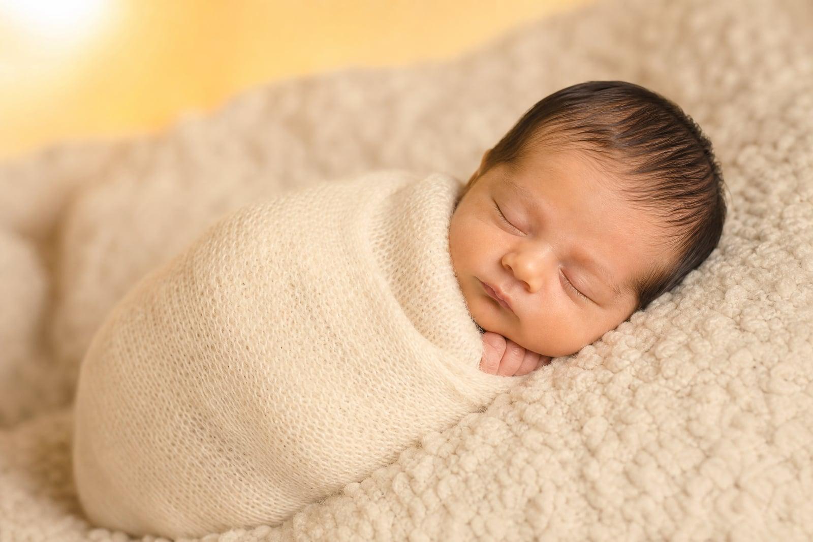 Newborn Photoshoot portrait of a sleeping baby in a cream knit wrap on a soft blanket